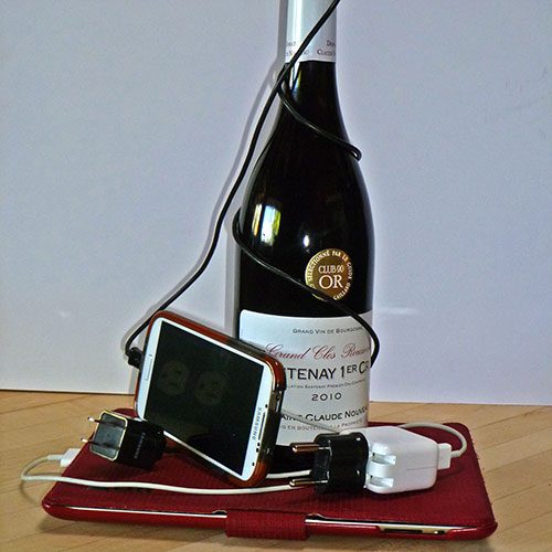 A French wine bottle with mobile phone, tablet and electrical cords.